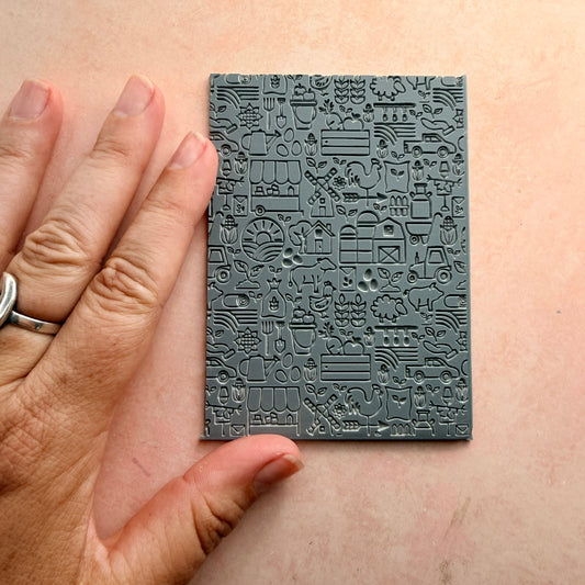 On the Farm 3x4 inch rubber stamp for polymer clay held next to hand showing full all-over farm icon design